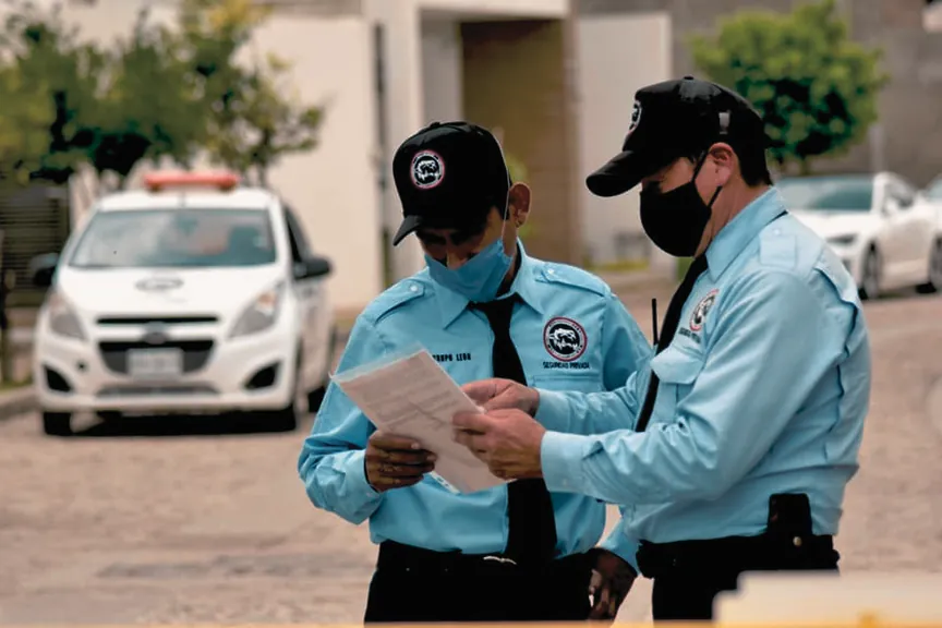 Dos oficiales de seguridad privada de Grupo León con uniforme azul revisando documentos junto a una patrulla
